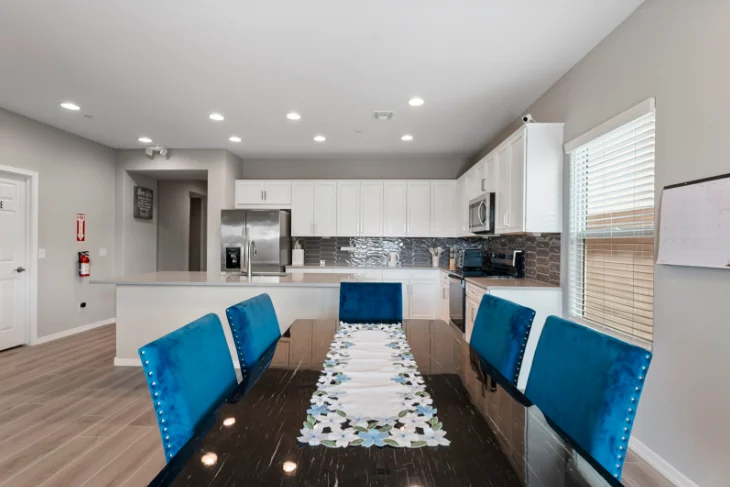 Dining area with blue chairs leading into the kitchen at Sunrise Haven Senior Homes