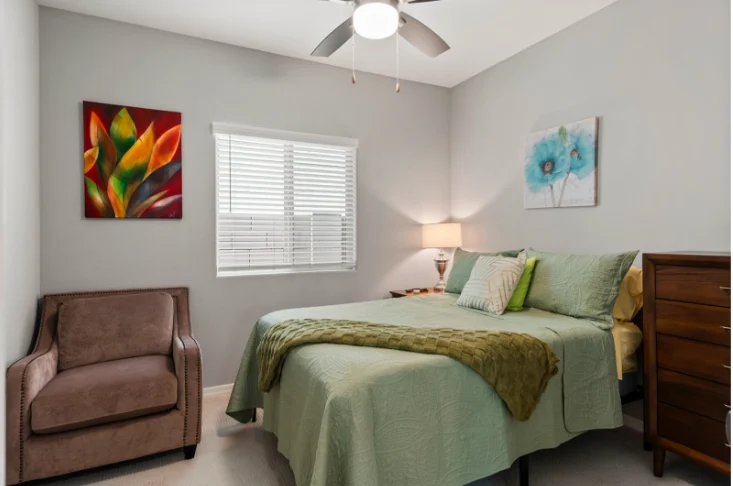 Resident bedroom with a full bed, armchair and ceiling fan at Sunrise Haven Senior Homes